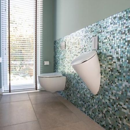 Badezimmer mit braun grauen Bodenfliesen in Stein-Optik und unterschiedlichen, kleinen, primär grünlichen Fliesen an der Wand etwa halbhoch zur Decke