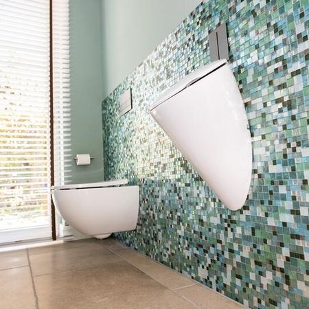 Badezimmer mit braun grauen Bodenfliesen in Stein-Optik und unterschiedlichen, kleinen, primär grünlichen Fliesen an der Wand etwa halbhoch zur Decke