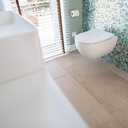 Badezimmer mit braun grauen Bodenfliesen in Stein-Optik und unterschiedlichen, kleinen, primär grünlichen Fliesen an der Wand etwa halbhoch zur Decke