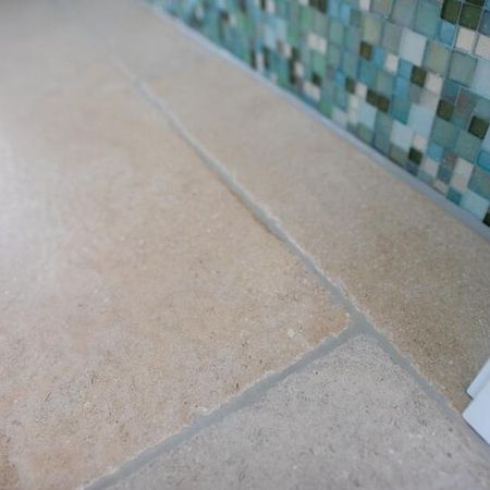 Badezimmer mit braun grauen Bodenfliesen in Stein-Optik und unterschiedlichen, kleinen, primär grünlichen Fliesen an der Wand etwa halbhoch zur Decke