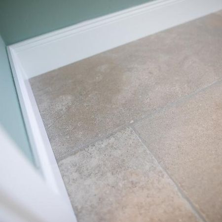 Badezimmer mit braun grauen Bodenfliesen in Stein-Optik und unterschiedlichen, kleinen, primär grünlichen Fliesen an der Wand etwa halbhoch zur Decke