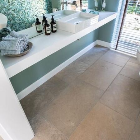 Badezimmer mit braun grauen Bodenfliesen in Stein-Optik und unterschiedlichen, kleinen, primär grünlichen Fliesen an der Wand etwa halbhoch zur Decke