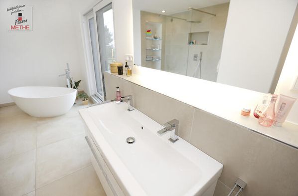 In einem weißen Badezimmer mit hellen Bodenfliesen steht eine weiße Badewanne